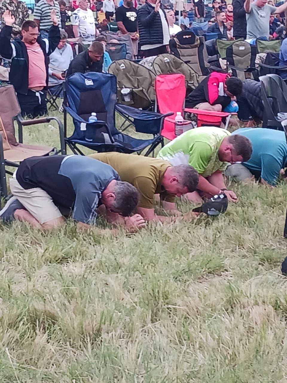 Men kneeling face-down in prayer on the grass